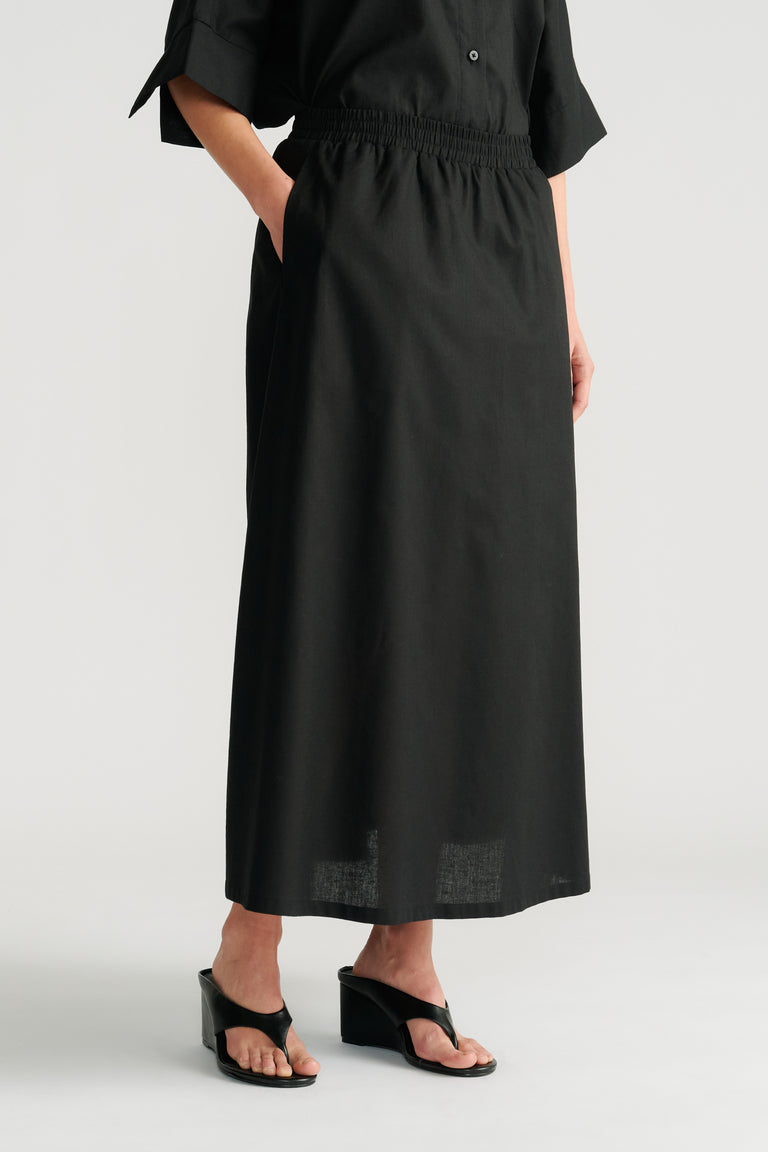 Woman wearing a black midi skirt with an elastic waistband paired with black wedge sandals and a relaxed black top
