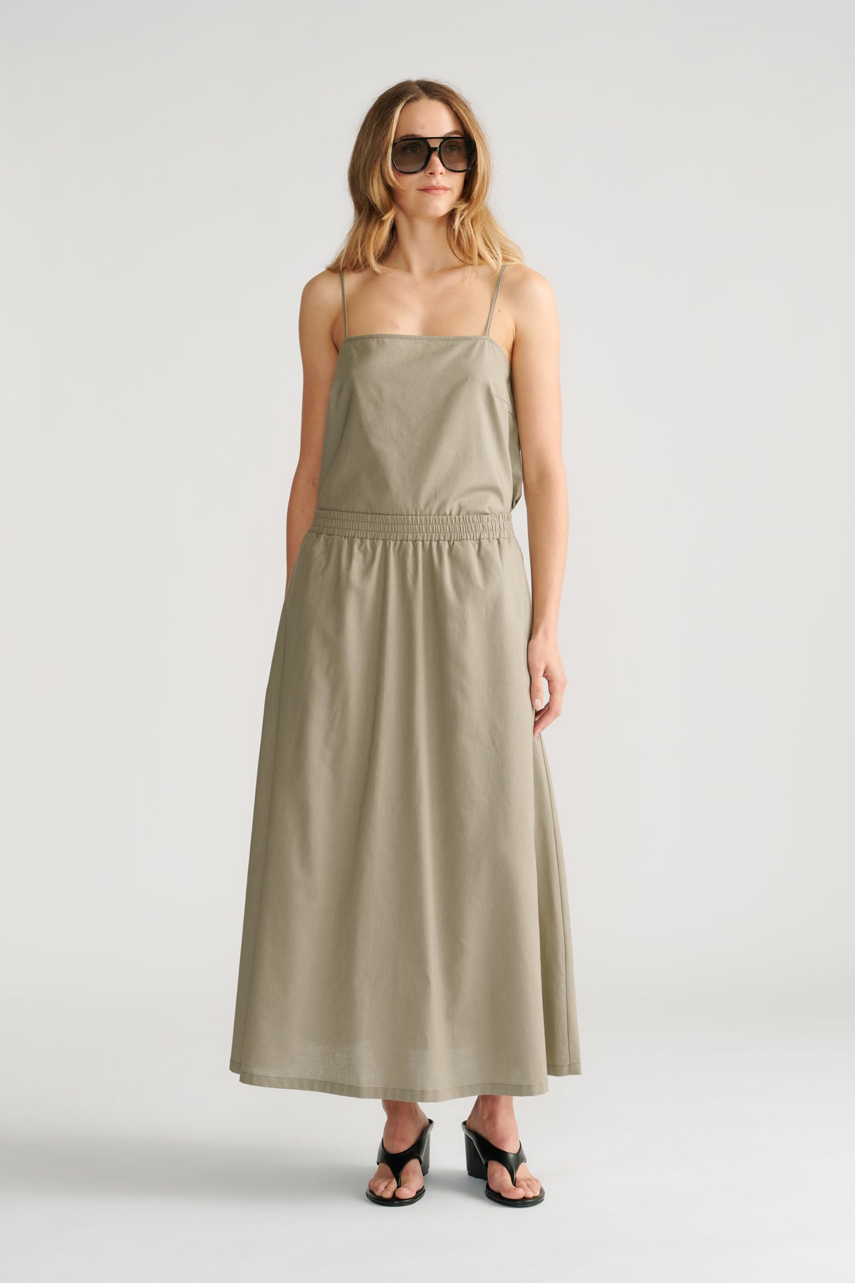 Woman wearing a sage green midi skirt with a fitted waist and spaghetti strap top, styled with black heeled sandals.