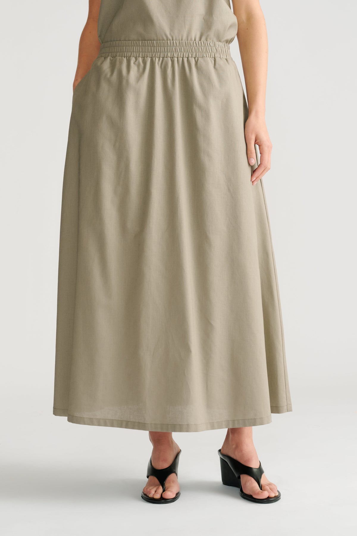 Woman wearing a relaxed fit sage midi skirt with an elastic waistband paired with black heeled sandals.