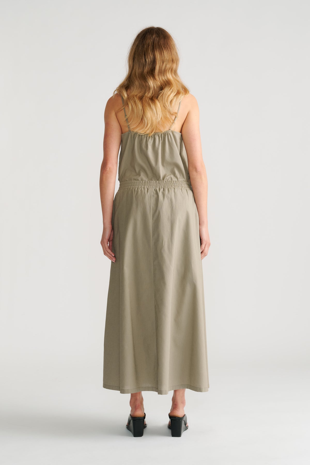 Woman seen from behind wearing a sage green midi skirt with an elastic waist and matching sleeveless top.