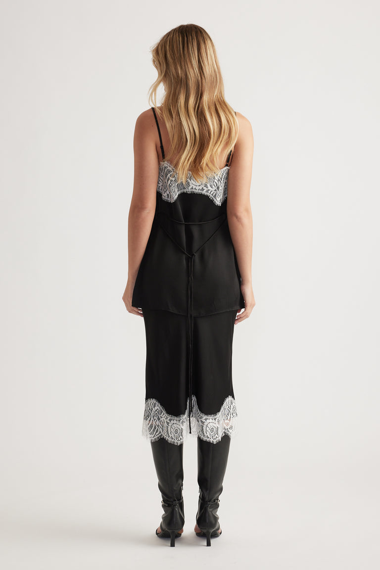 Woman wearing a black slip dress with white lace trim on the back and hem, paired with black high boots.