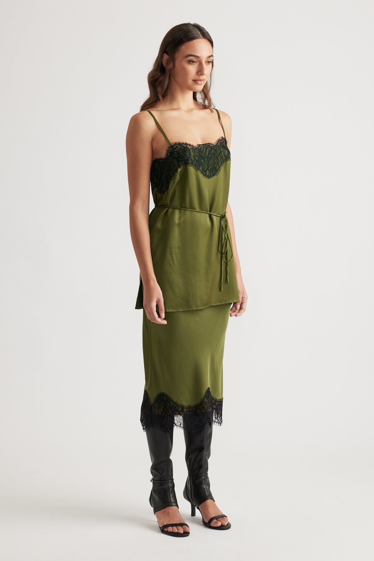 Olive green slip dress with black lace trim and delicate straps paired with knee-high black leather boots.