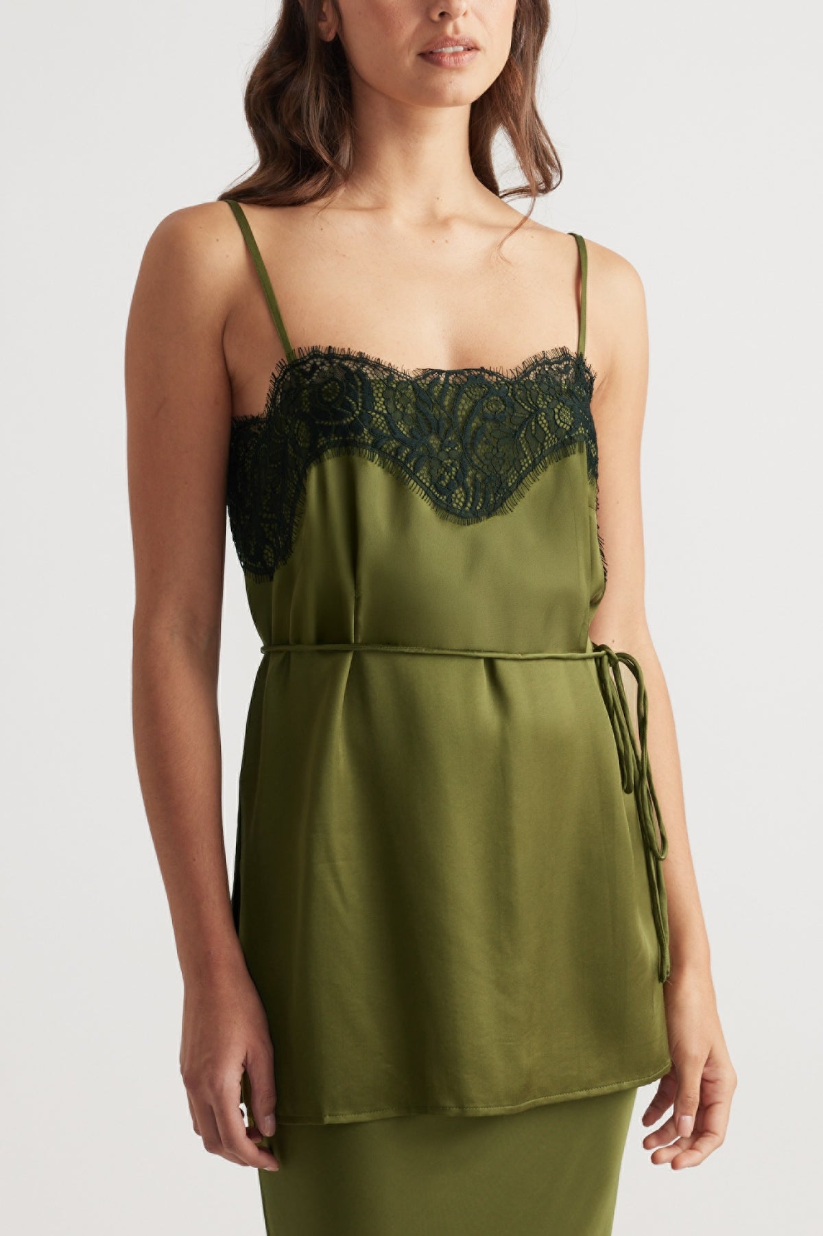 Woman wearing an olive green satin camisole with delicate black lace trim and thin adjustable straps.