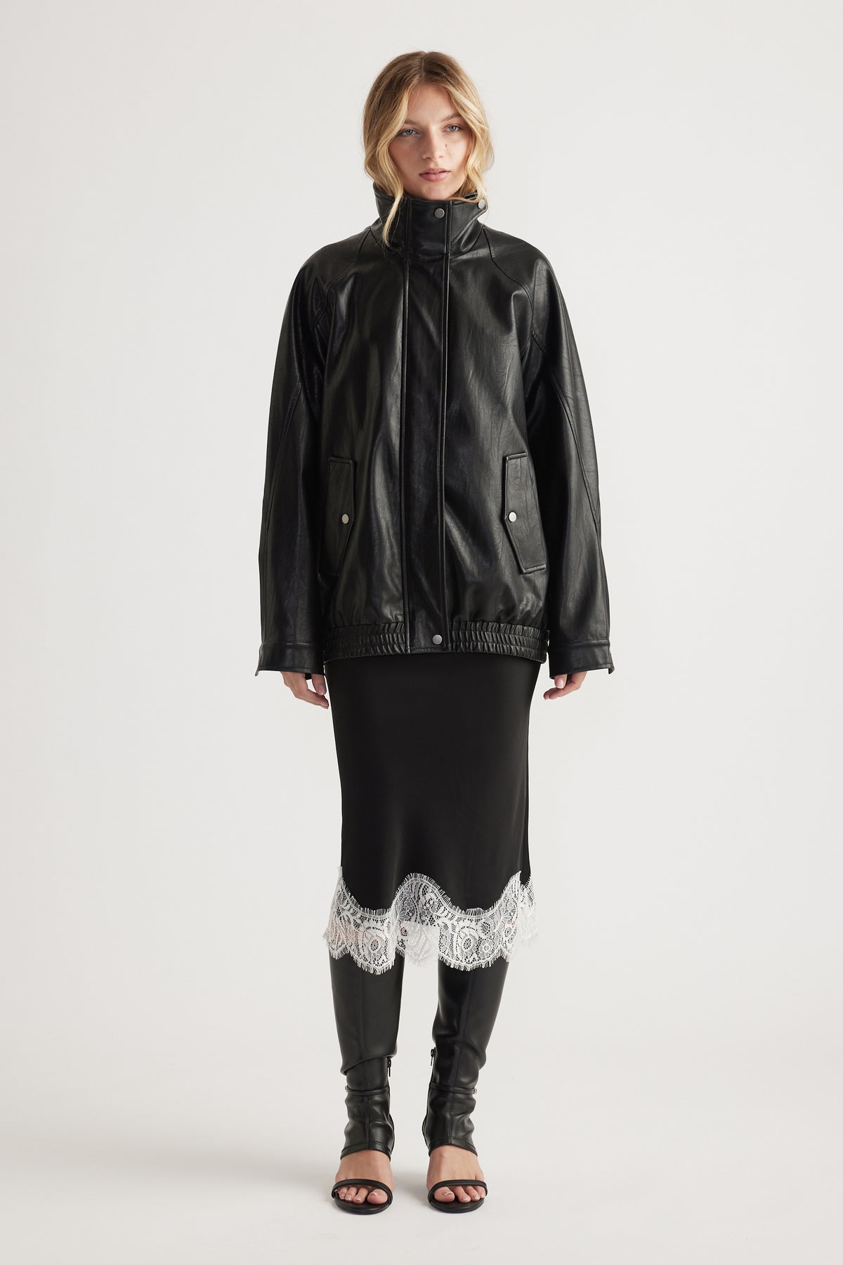Woman wearing a black midi skirt with white lace trim paired with a black leather jacket and open-toe boots