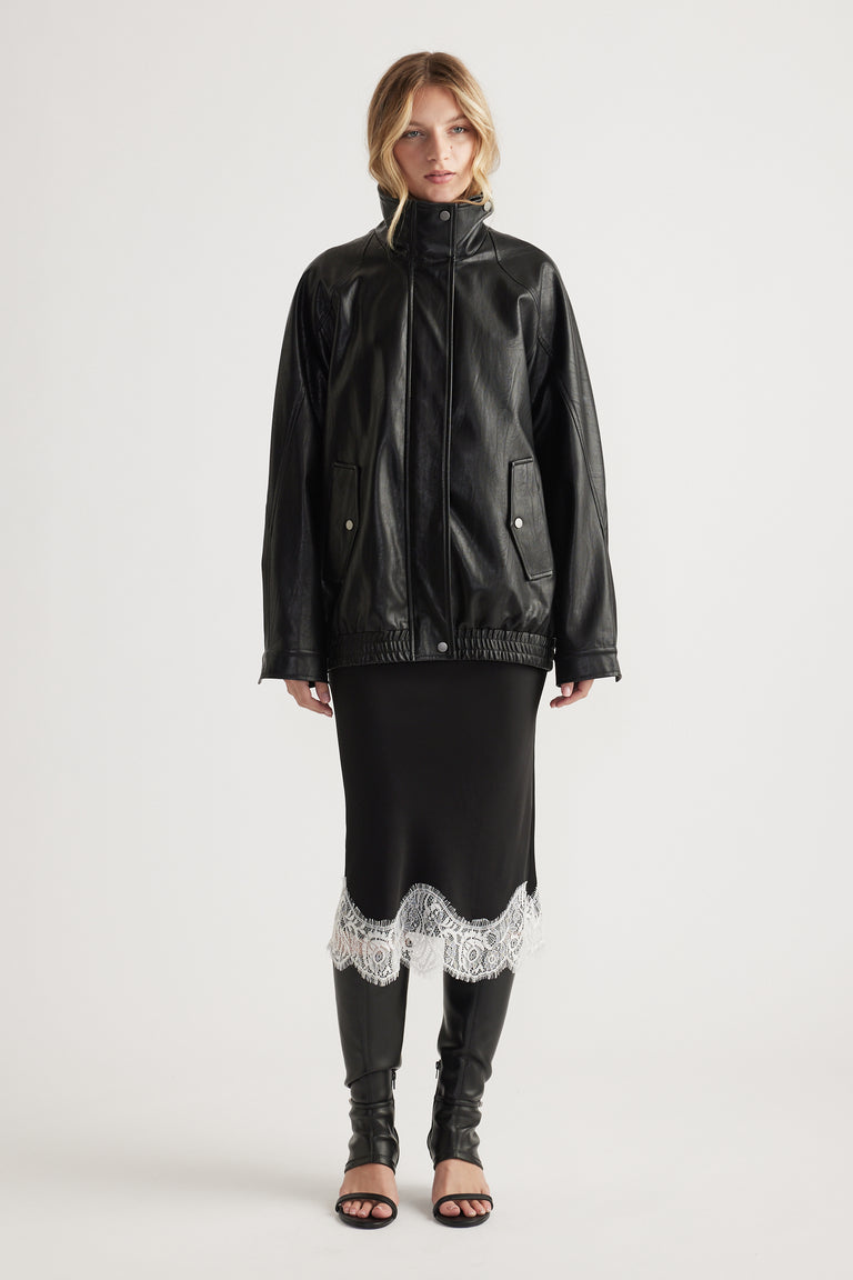 Woman wearing a black midi skirt with white lace trim paired with a black leather jacket and open-toe boots