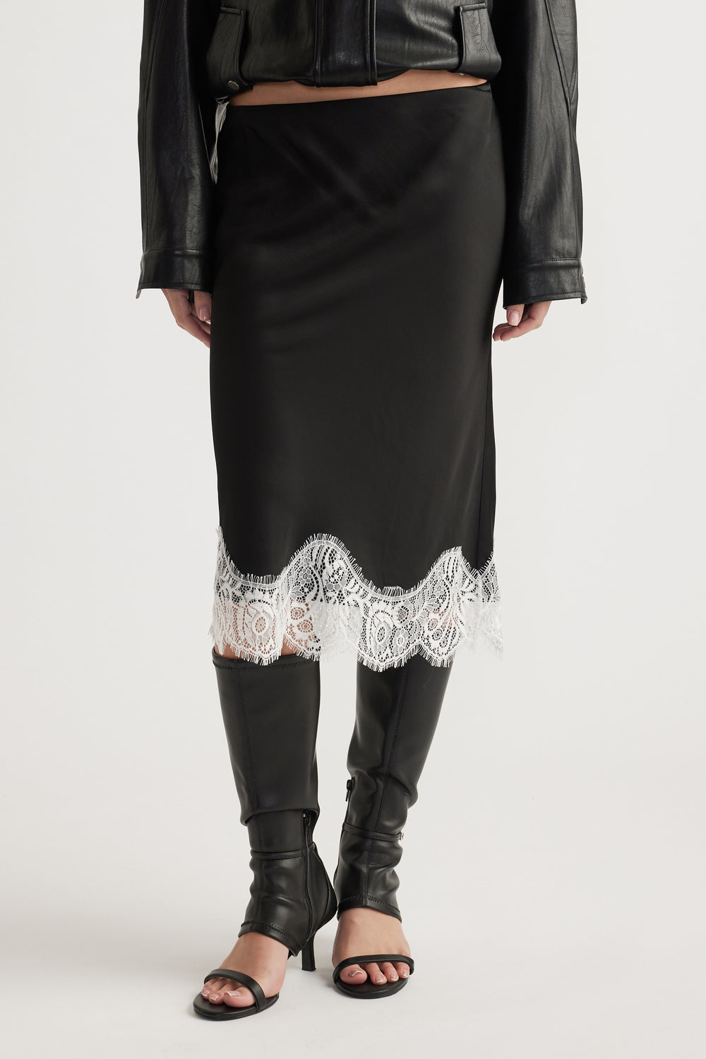 Black midi skirt with intricate white lace trim paired with knee-high black leather boots and a cropped jacket