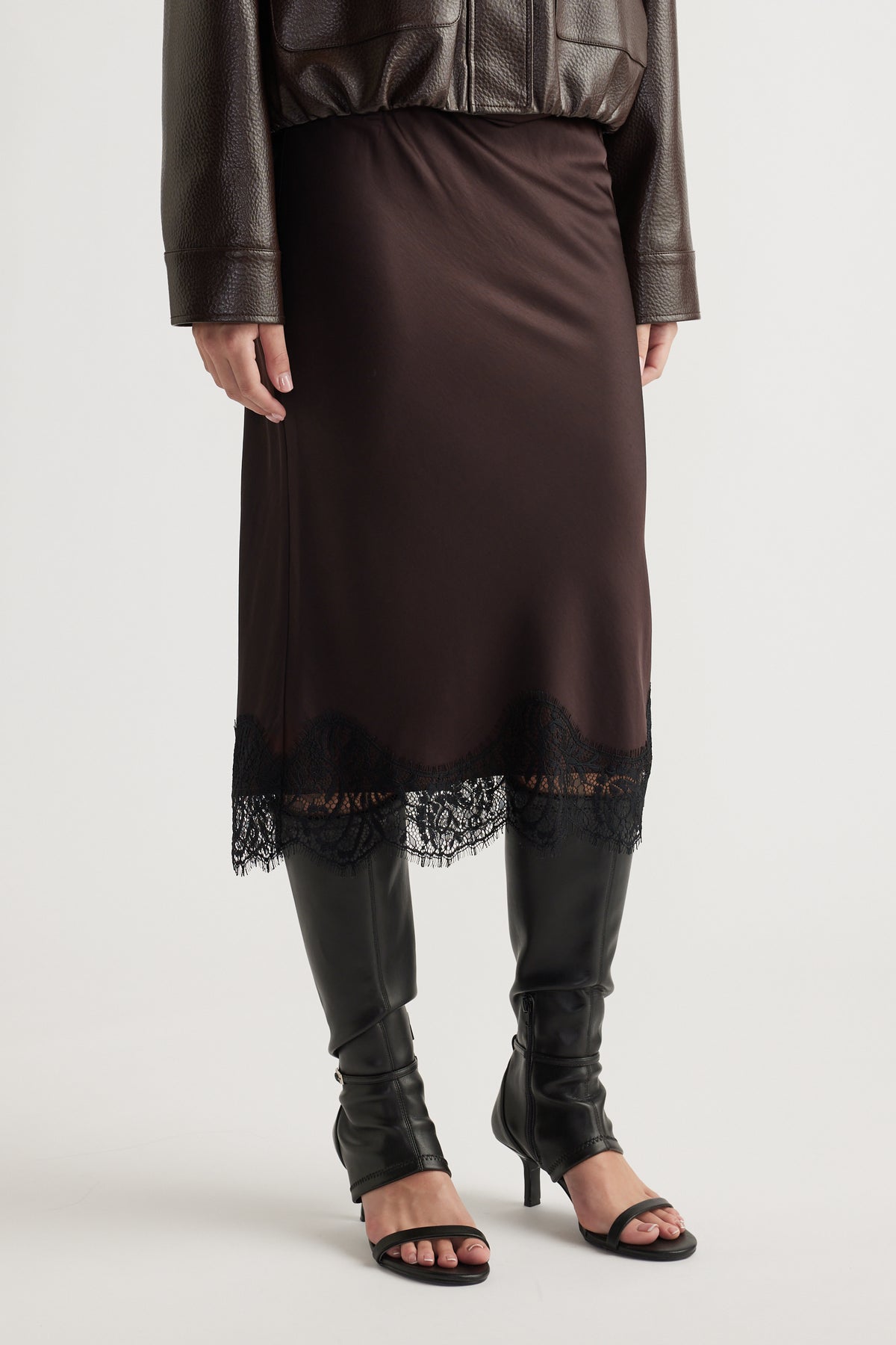 Woman wearing a dark brown skirt with delicate black lace trim paired with black heeled boots and a leather jacket.
