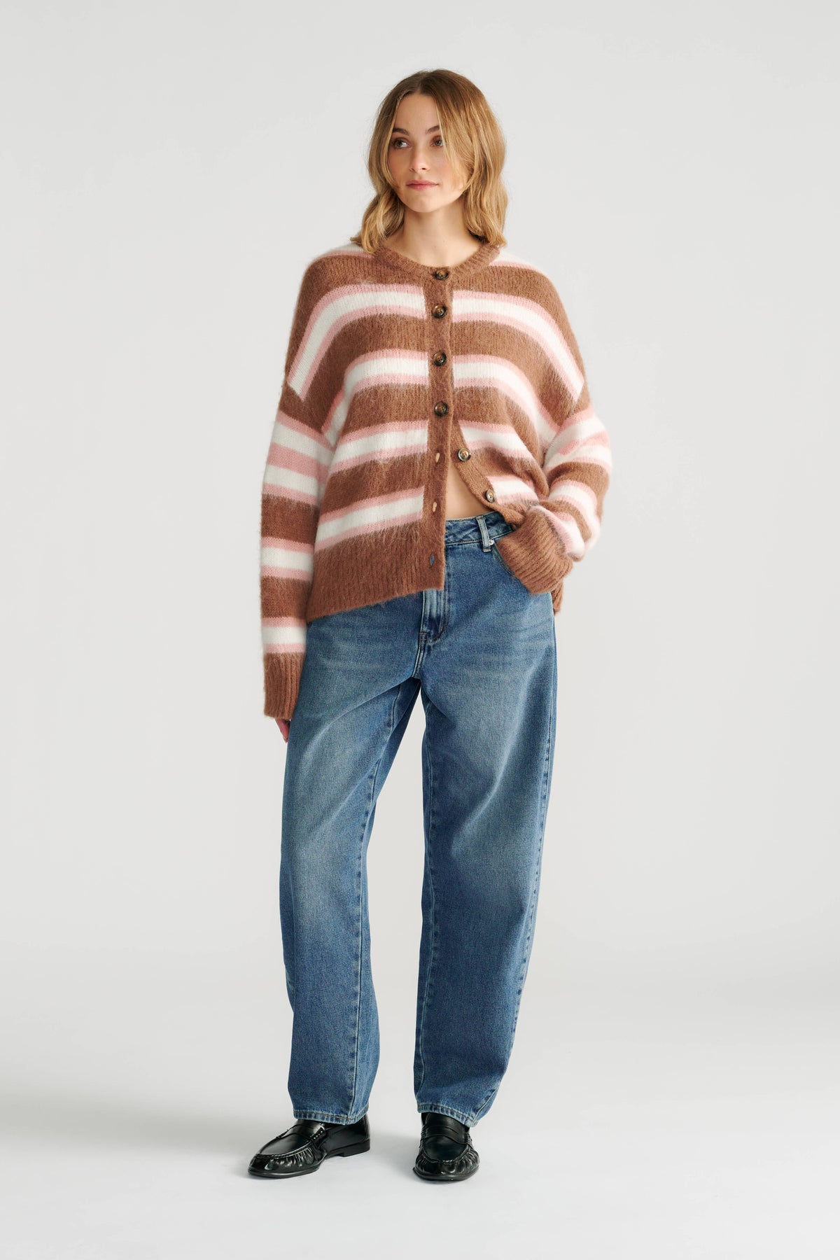 Woman wearing a cozy striped cardigan in warm tones paired with relaxed-fit blue jeans and black loafers.