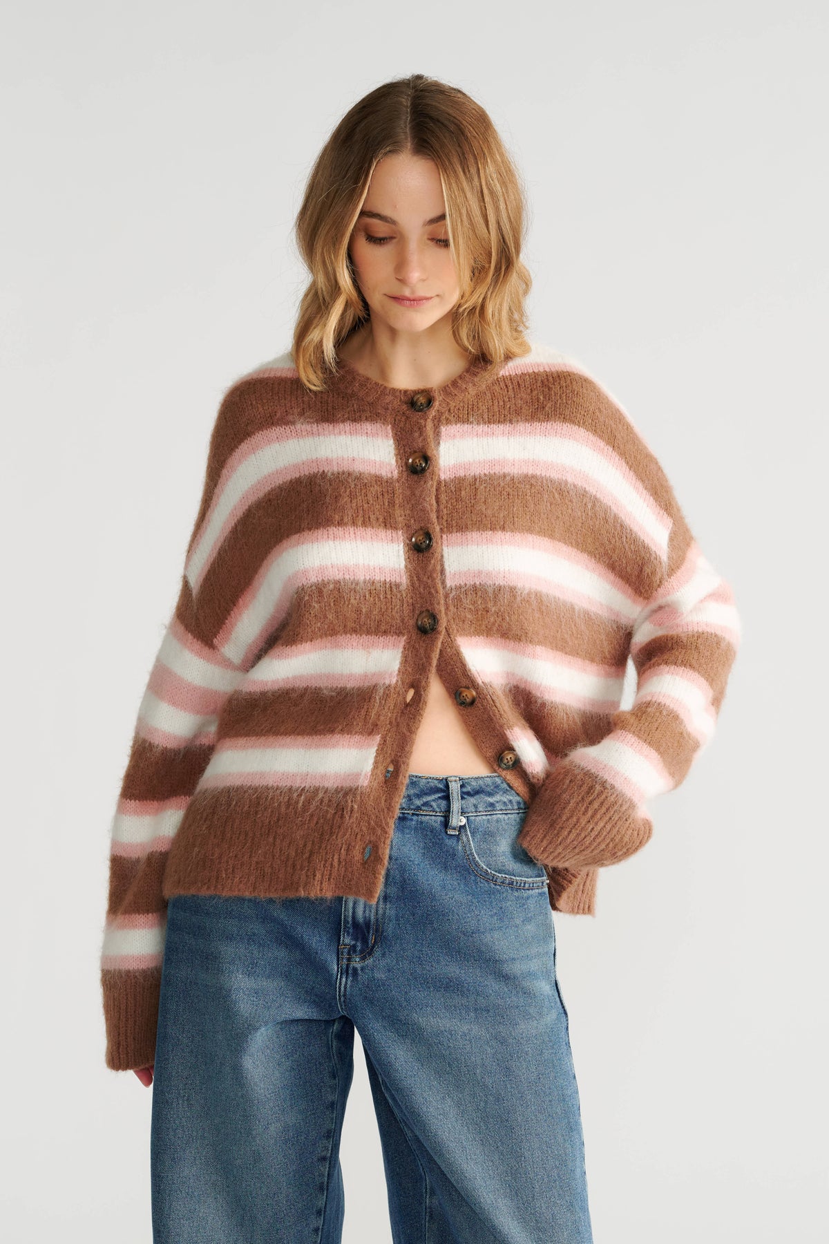Woman wearing a cozy striped knit cardigan in warm tones paired with relaxed fit blue denim jeans.