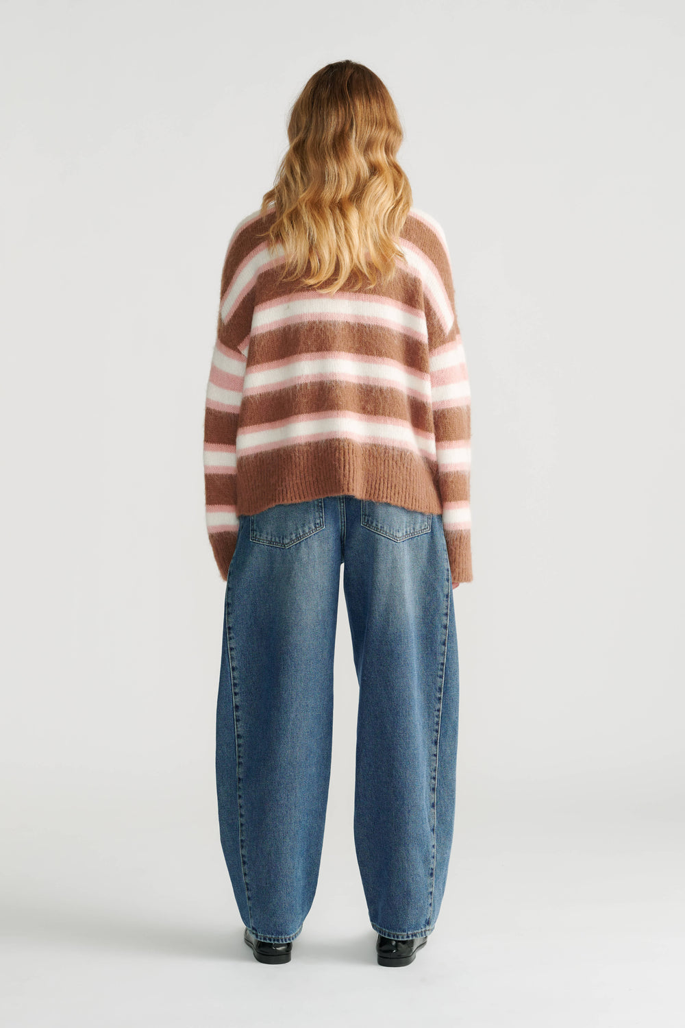 Woman wearing a relaxed soft striped knit cardigan in warm tones paired with loose wide-leg denim jeans, back view.
