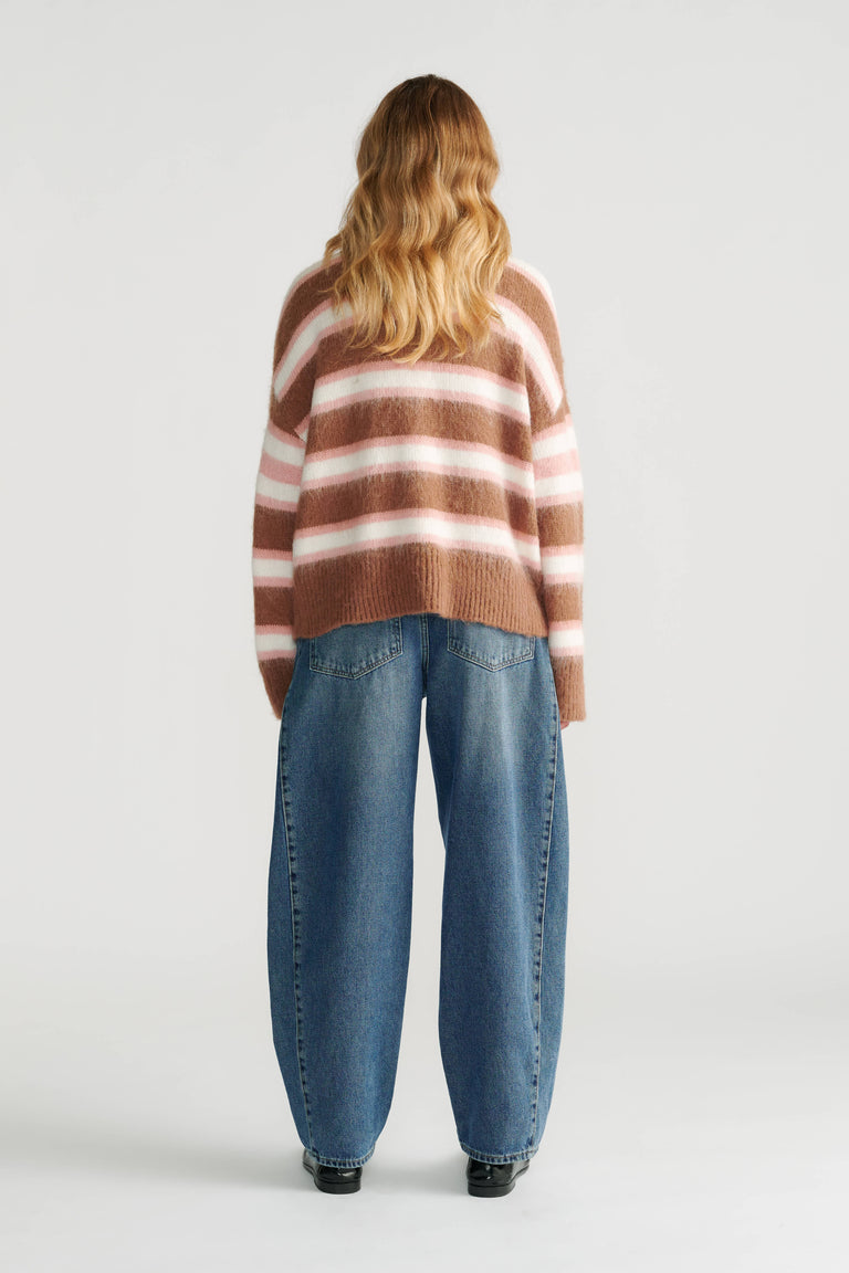 Woman wearing a relaxed soft striped knit cardigan in warm tones paired with loose wide-leg denim jeans, back view.