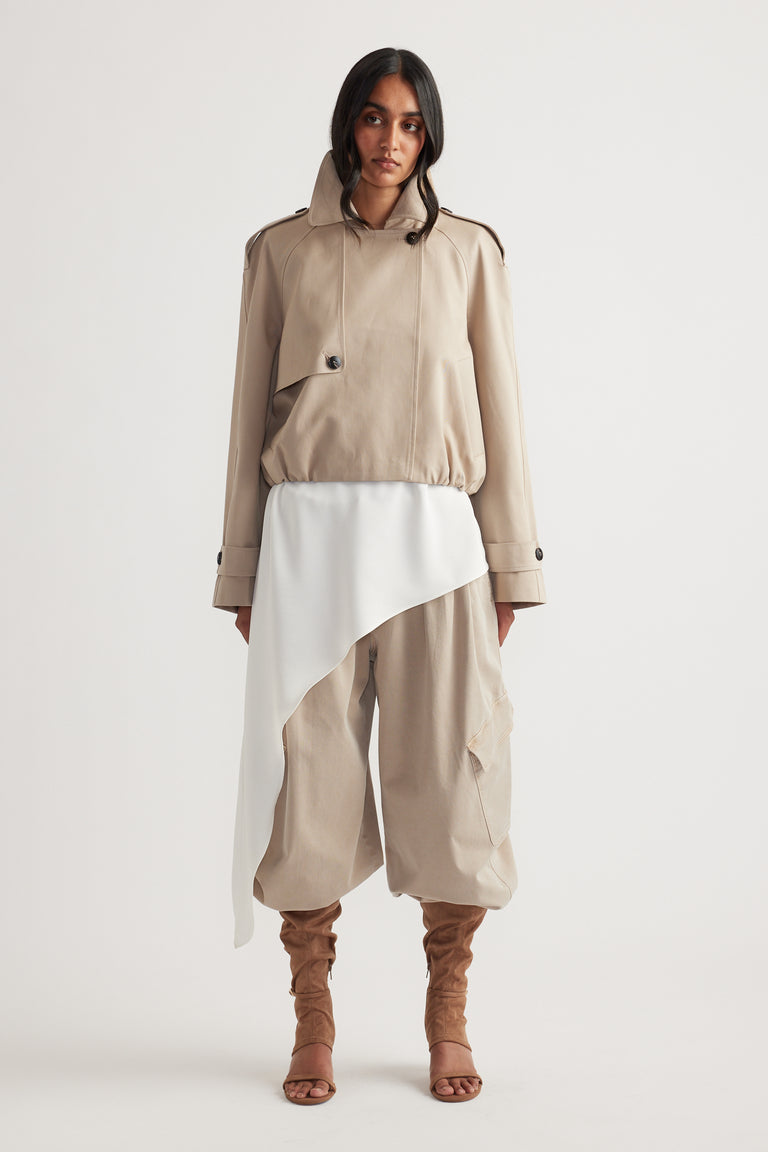 Woman wearing a cropped beige trench with bubble hem, paired with loose pants and ruched tan open-toe boots