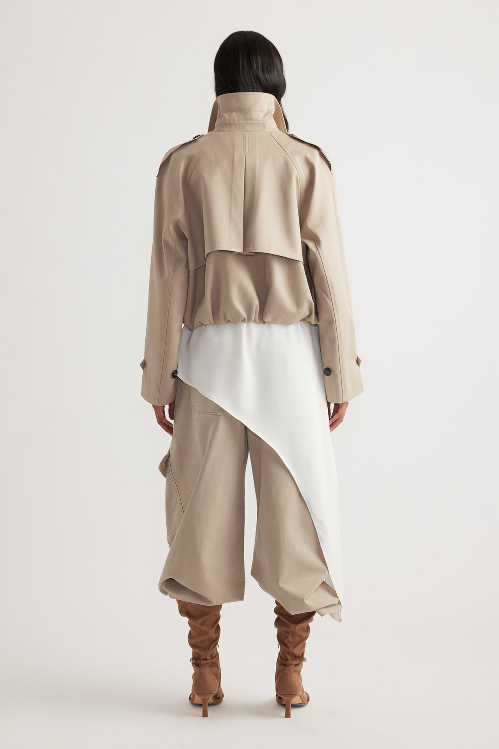 Woman seen from behind wearing a light beige cropped trench with puffed pants and slouchy brown heeled boots