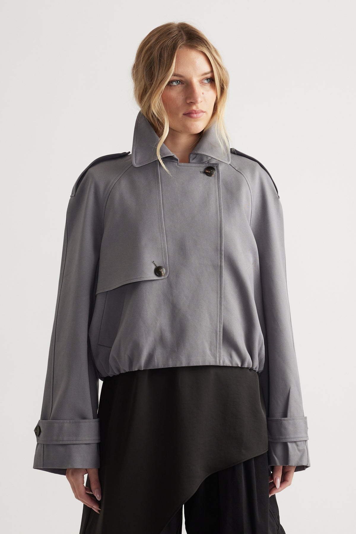 Woman wearing a soft grey bubble trench coat with oversized cuffs paired with a flowing black skirt for a chic look