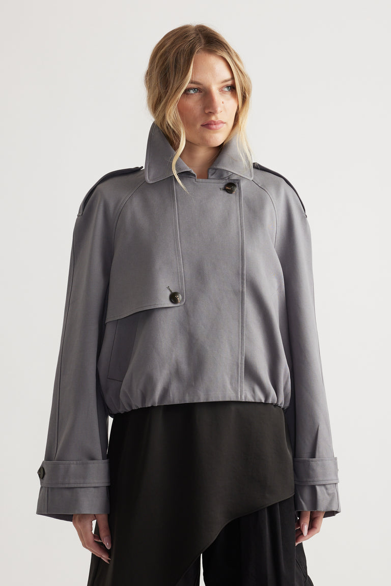 Woman wearing a soft grey bubble trench coat with oversized cuffs paired with a flowing black skirt for a chic look
