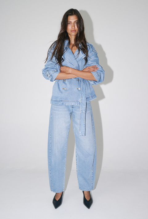 Woman wearing a light blue cropped denim trench coat with a belted waist, wide-leg jeans and black pointed shoes