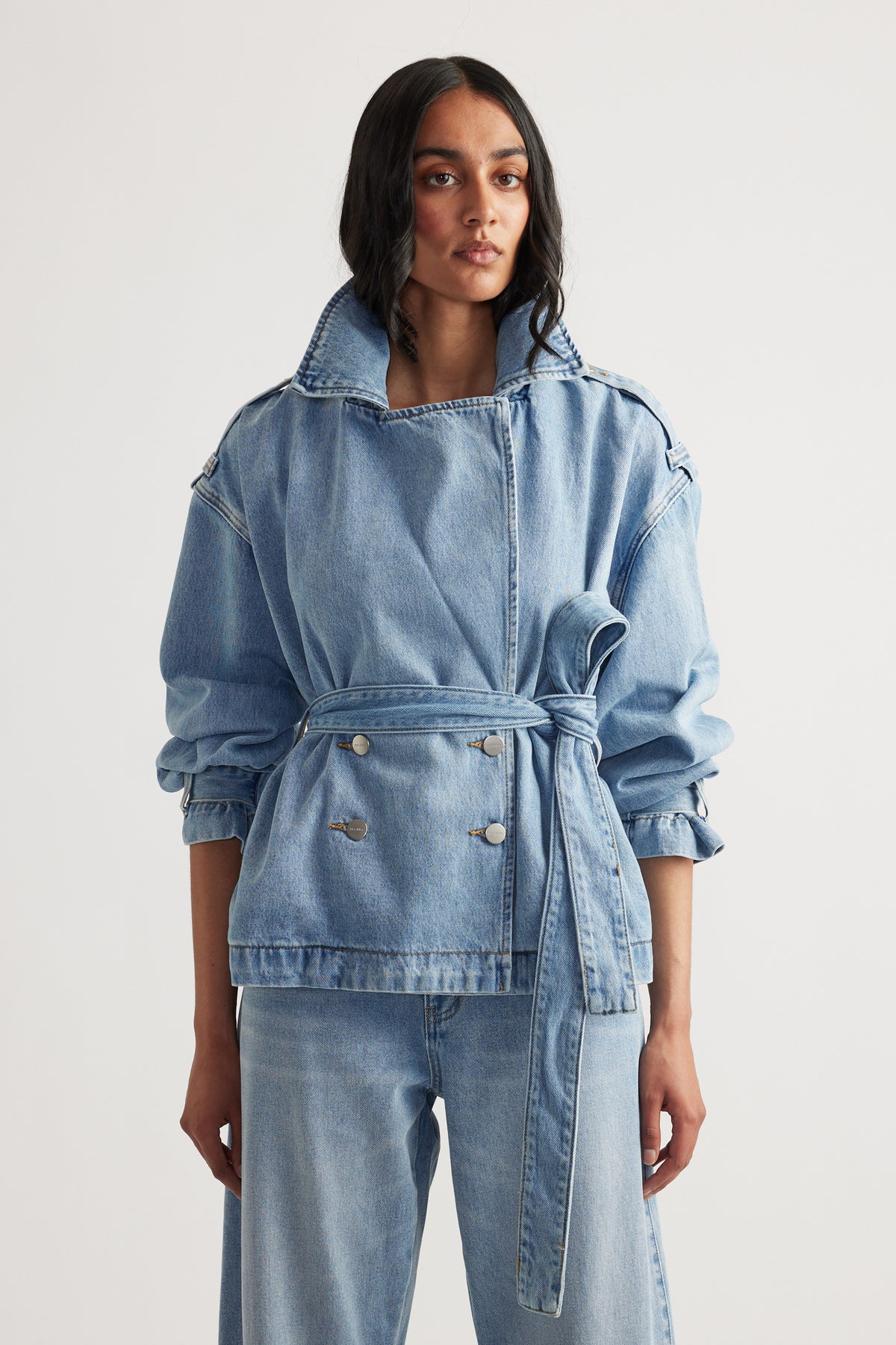 Woman wearing a belted light wash denim trench jacket with rolled sleeves and relaxed wide-leg denim jeans
