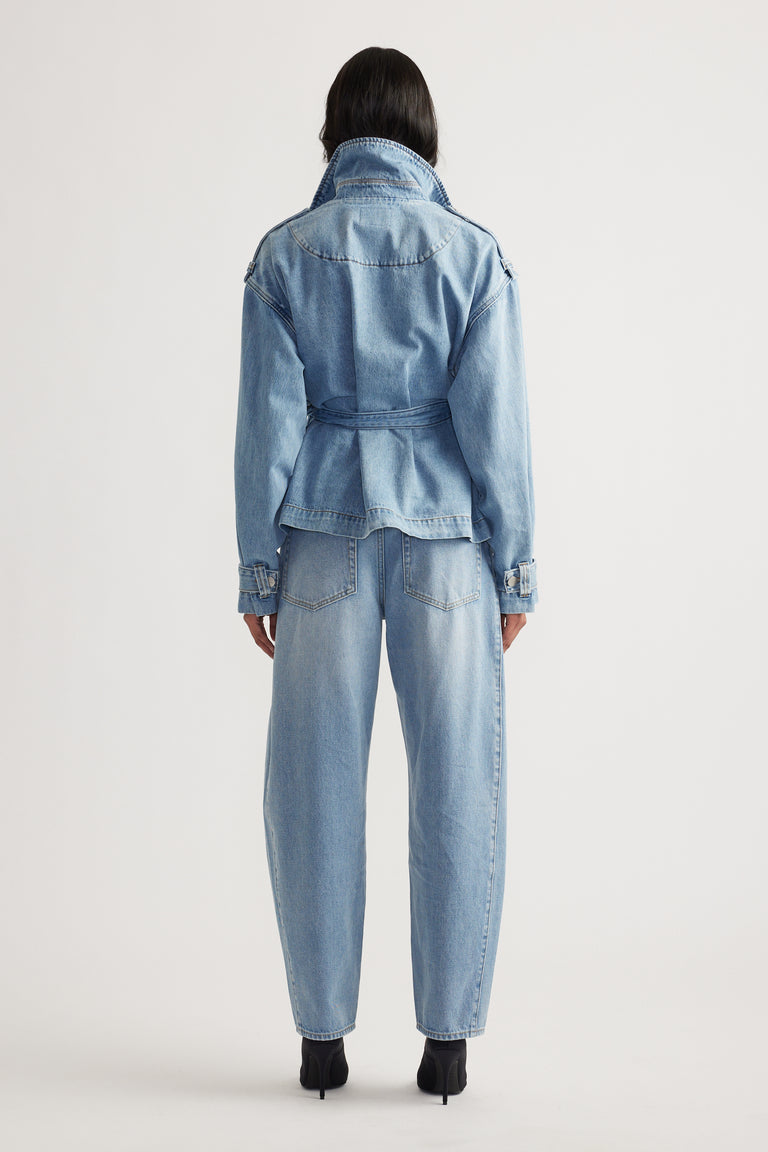 Woman seen from behind wearing a belted light wash denim jacket with a flared hem and matching high-waisted jeans