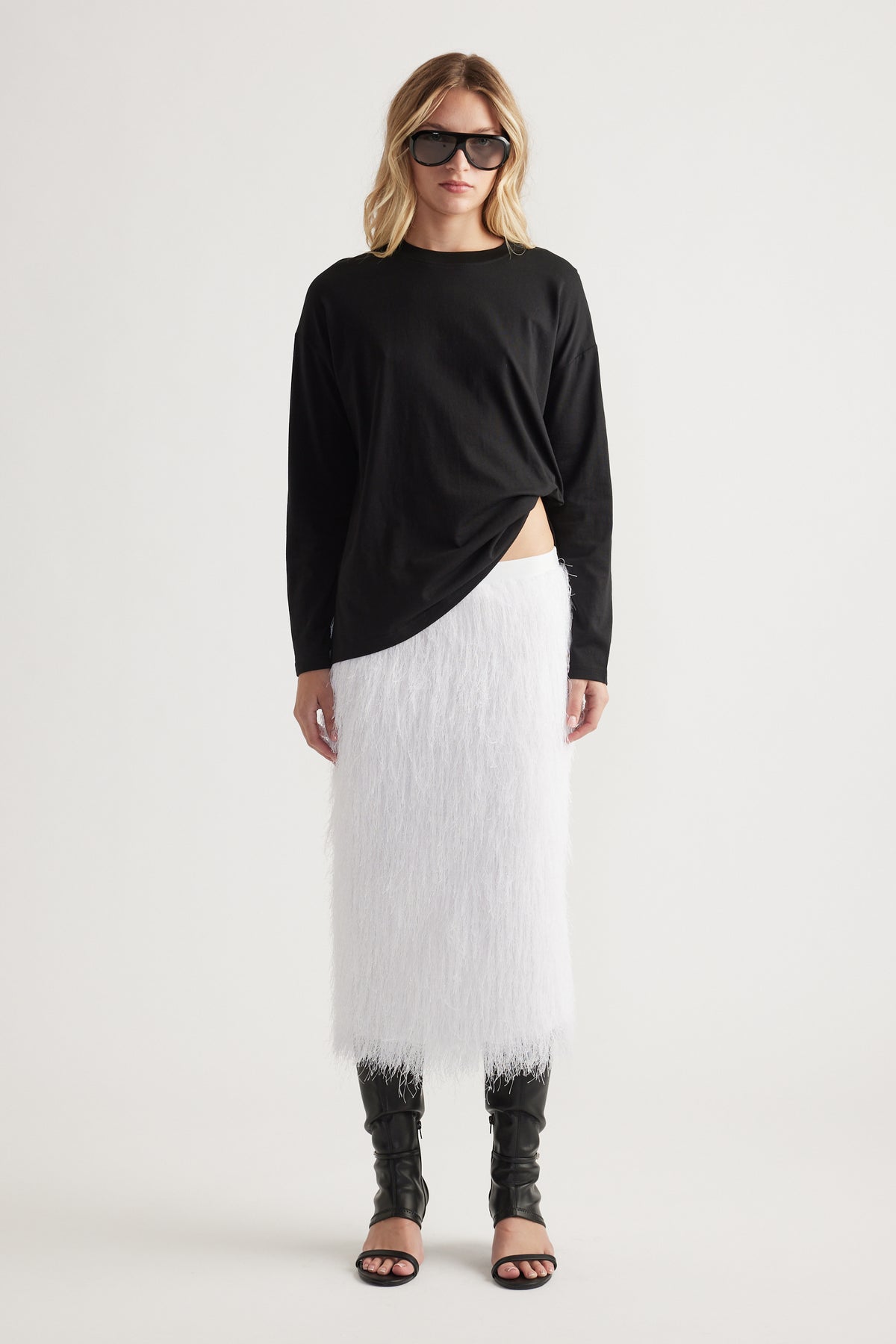 Woman wearing a relaxed black crew neck long sleeve top paired with a textured white midi skirt and black open-toe boots