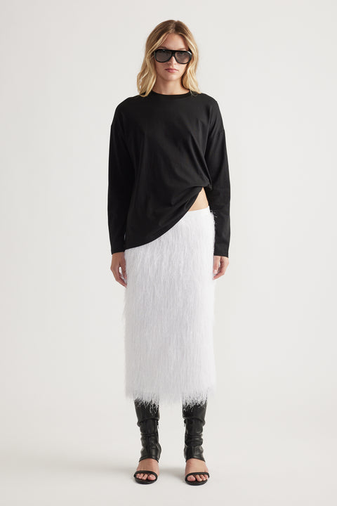 Woman wearing a relaxed black crew neck long sleeve top paired with a textured white midi skirt and black open-toe boots