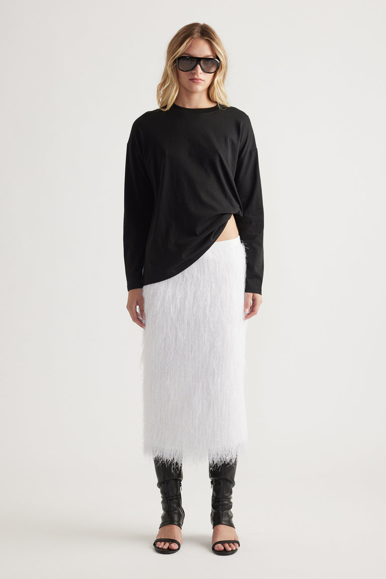 Woman wearing a relaxed black crew neck long sleeve top paired with a textured white midi skirt and black open-toe boots