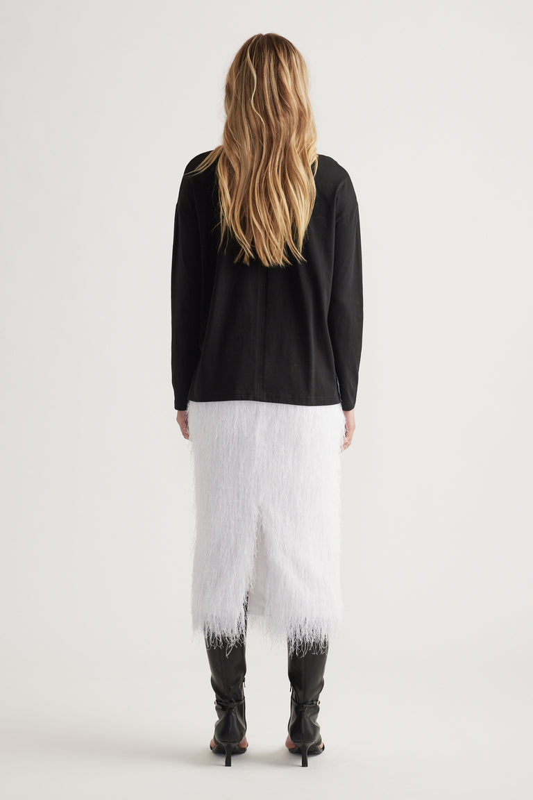 Woman wearing a black long sleeve top paired with a textured white midi skirt and black heeled boots, viewed from behind.