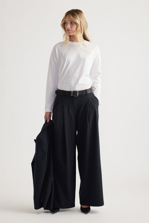 Woman wearing a white long sleeve top tucked into high-waisted wide-leg black pants, holding a matching blazer.