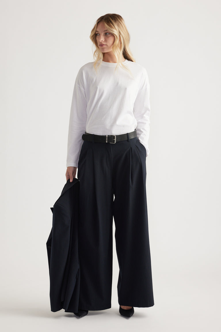 Woman wearing a white long sleeve top tucked into high-waisted wide-leg black pants, holding a matching blazer.