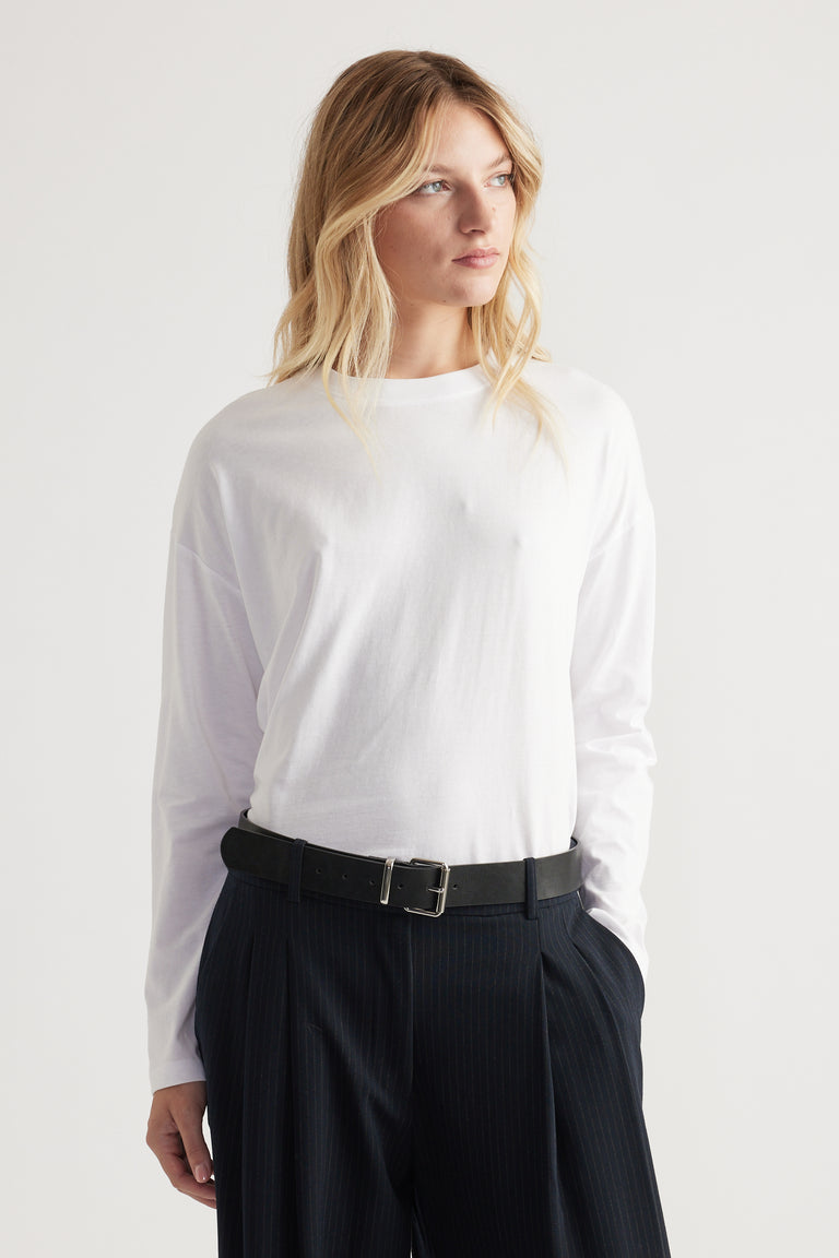 Woman wearing a crisp white long sleeve crew neck top tucked into high-waisted pinstripe pants with a black belt.