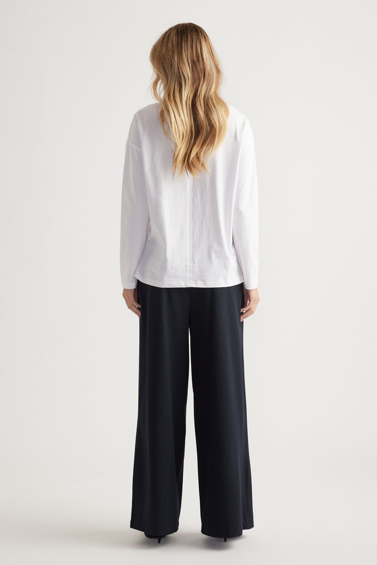 Woman wearing a relaxed white long-sleeve top paired with wide-leg black pants in a clean minimal studio setting