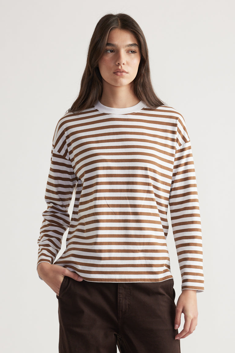 Woman wearing a relaxed fit crew neck long sleeve top with brown and white horizontal stripes paired with dark pants.