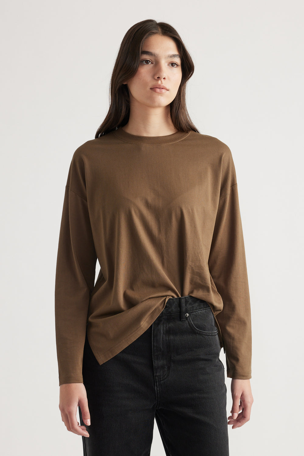 Woman wearing a relaxed bronze long-sleeve crew neck top paired with high-waisted black jeans, styled casually.