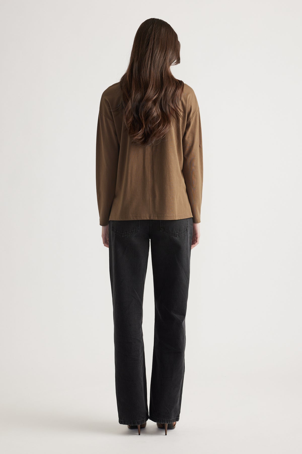 Woman seen from behind wearing a relaxed bronze crew neck long sleeve top with straight black denim jeans and heels