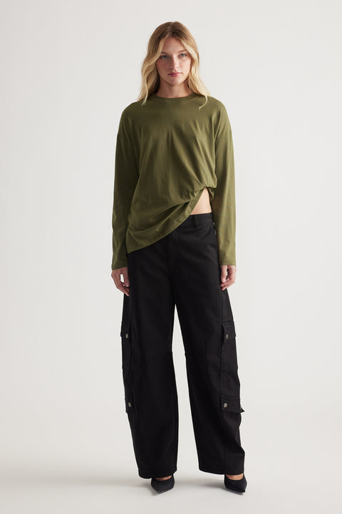 Woman wearing an olive green long sleeve top with black wide-leg cargo pants and black pointed flats in a neutral studio setting