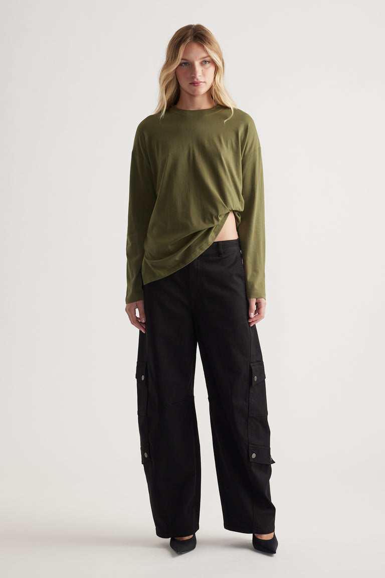 Woman wearing an olive green long sleeve top with black wide-leg cargo pants and black pointed flats in a neutral studio setting