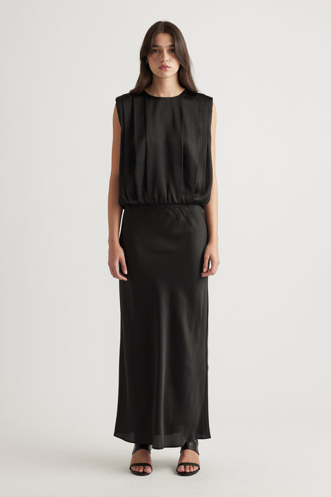 Woman wearing a sleeveless black satin dress with a relaxed top and fitted long skirt, styled with black open-toe heels