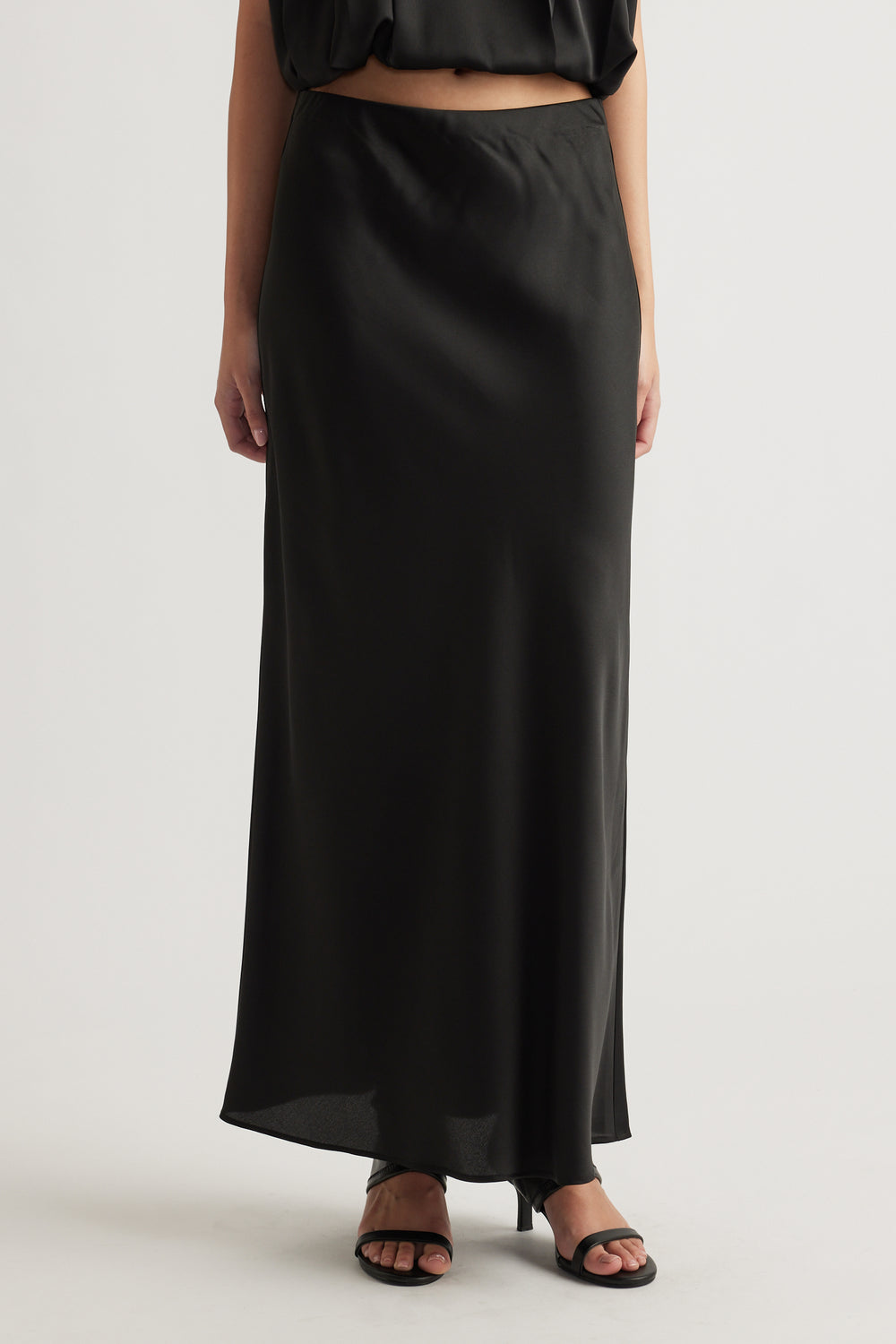 Woman wearing a sleek black satin maxi skirt paired with strappy black heels for a refined, effortless look