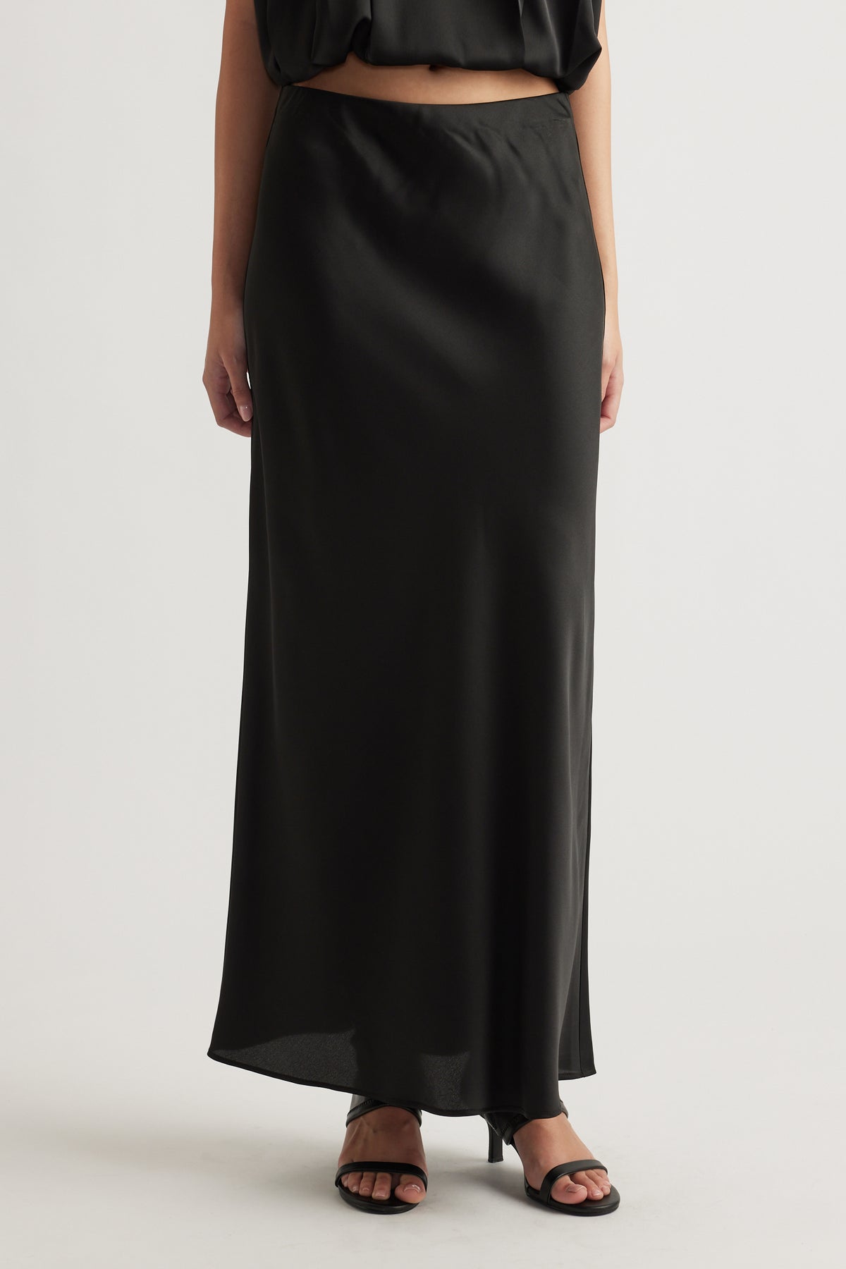 Woman wearing a sleek black satin maxi skirt paired with strappy black heels for a refined, effortless look