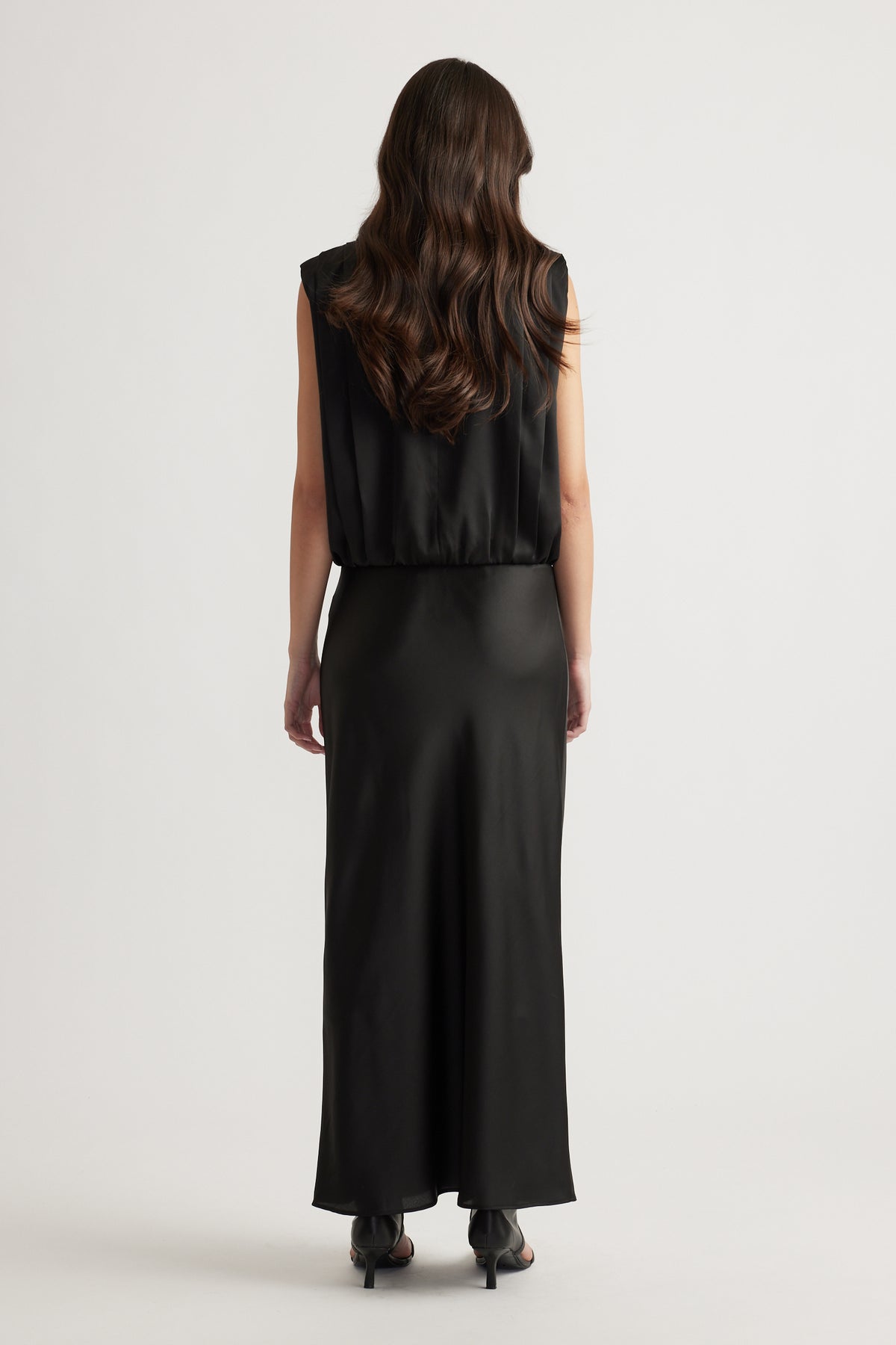 Woman wearing a sleek black satin skirt with a relaxed fit and sleeveless top, styled with black heels