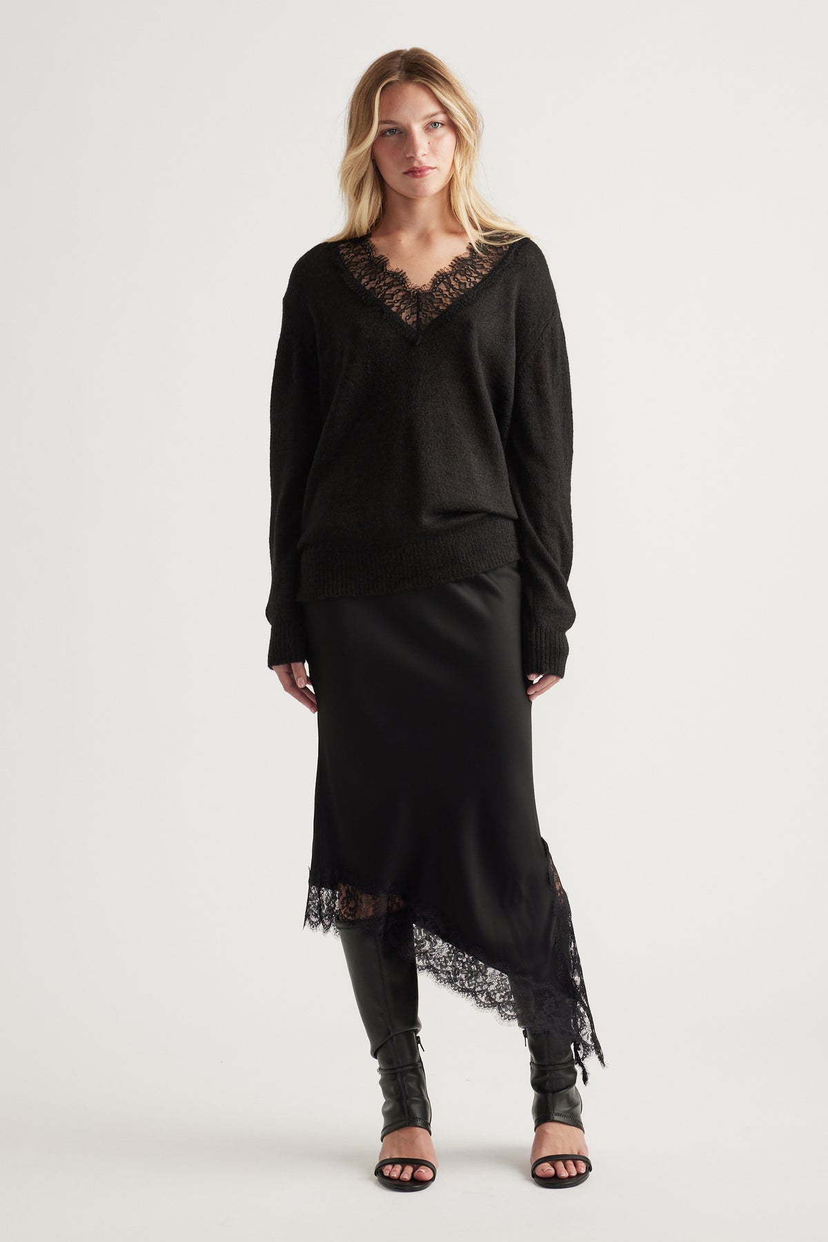 Woman wearing a black V-neck jumper with lace trim paired with a silky asymmetrical lace-hem skirt and black heels