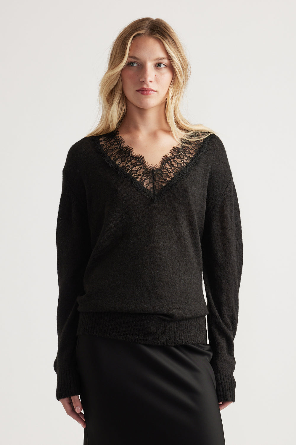 Woman wearing a soft black knit jumper with delicate lace-trimmed V neckline paired with a sleek black skirt
