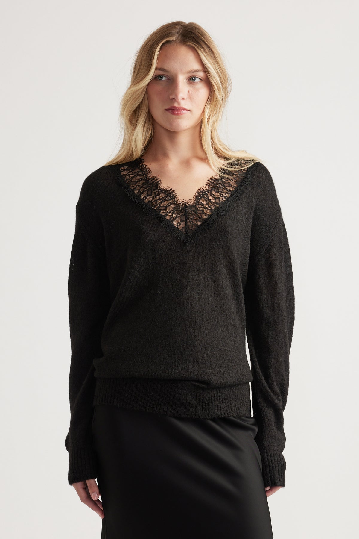 Woman wearing a soft black knit jumper with delicate lace-trimmed V neckline paired with a sleek black skirt