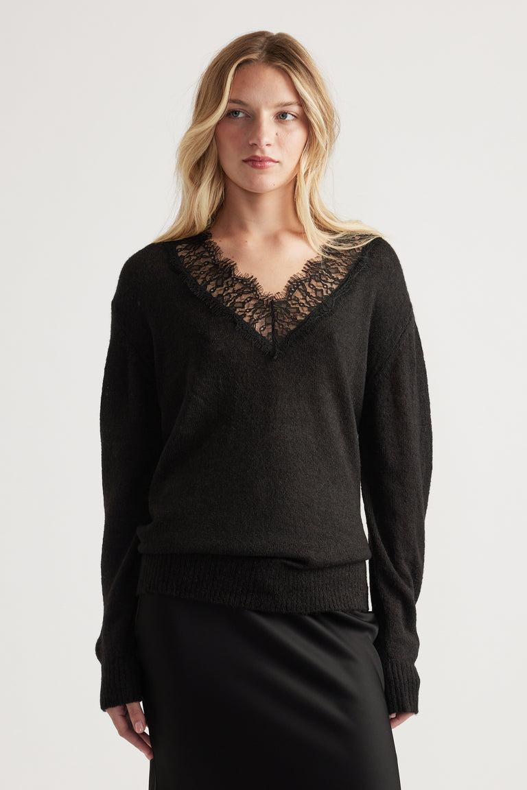 Woman wearing a soft black knit jumper with delicate lace-trimmed V neckline paired with a sleek black skirt