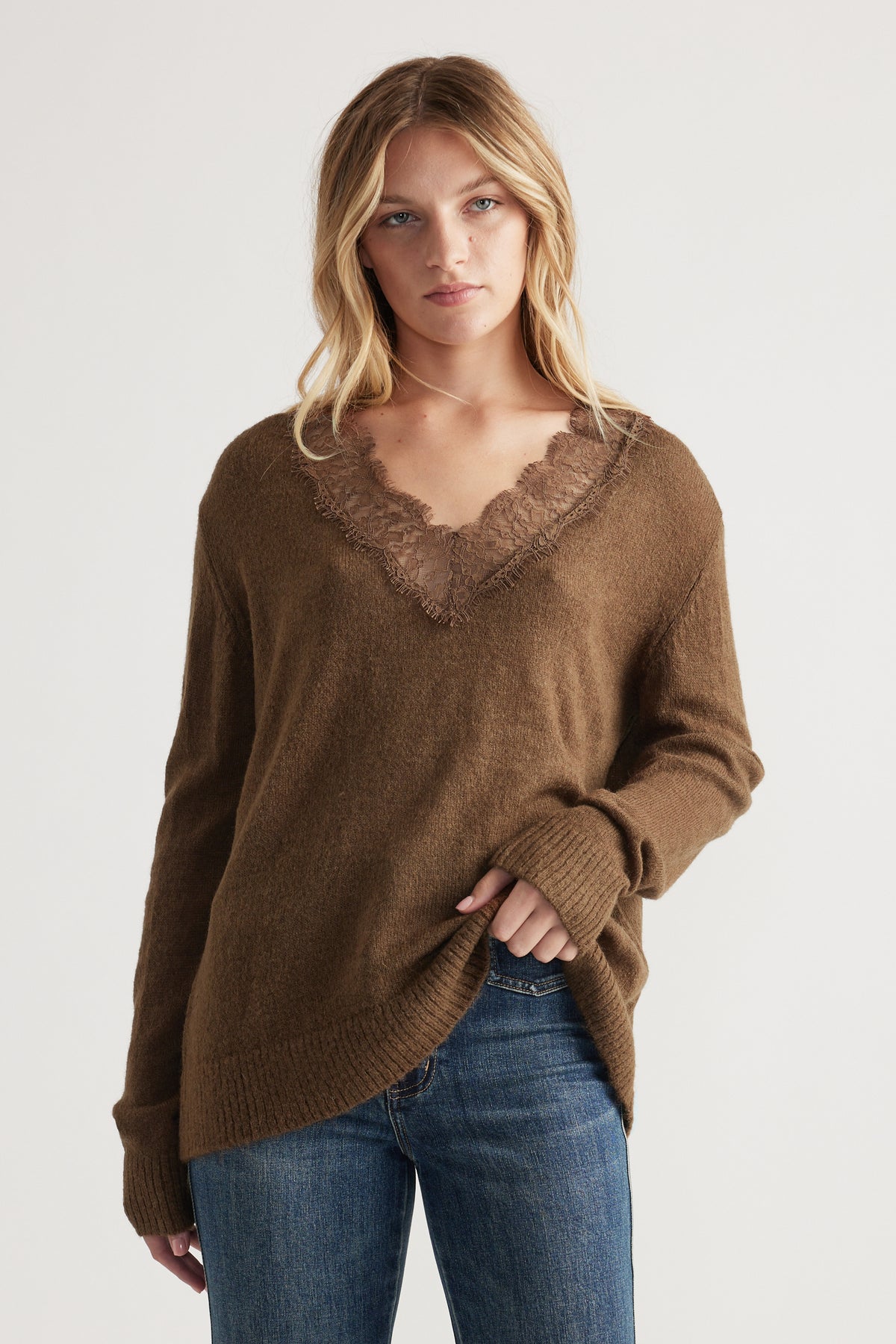 Woman wearing a relaxed brown knit sweater with lace-trimmed V-neck paired with classic blue denim jeans