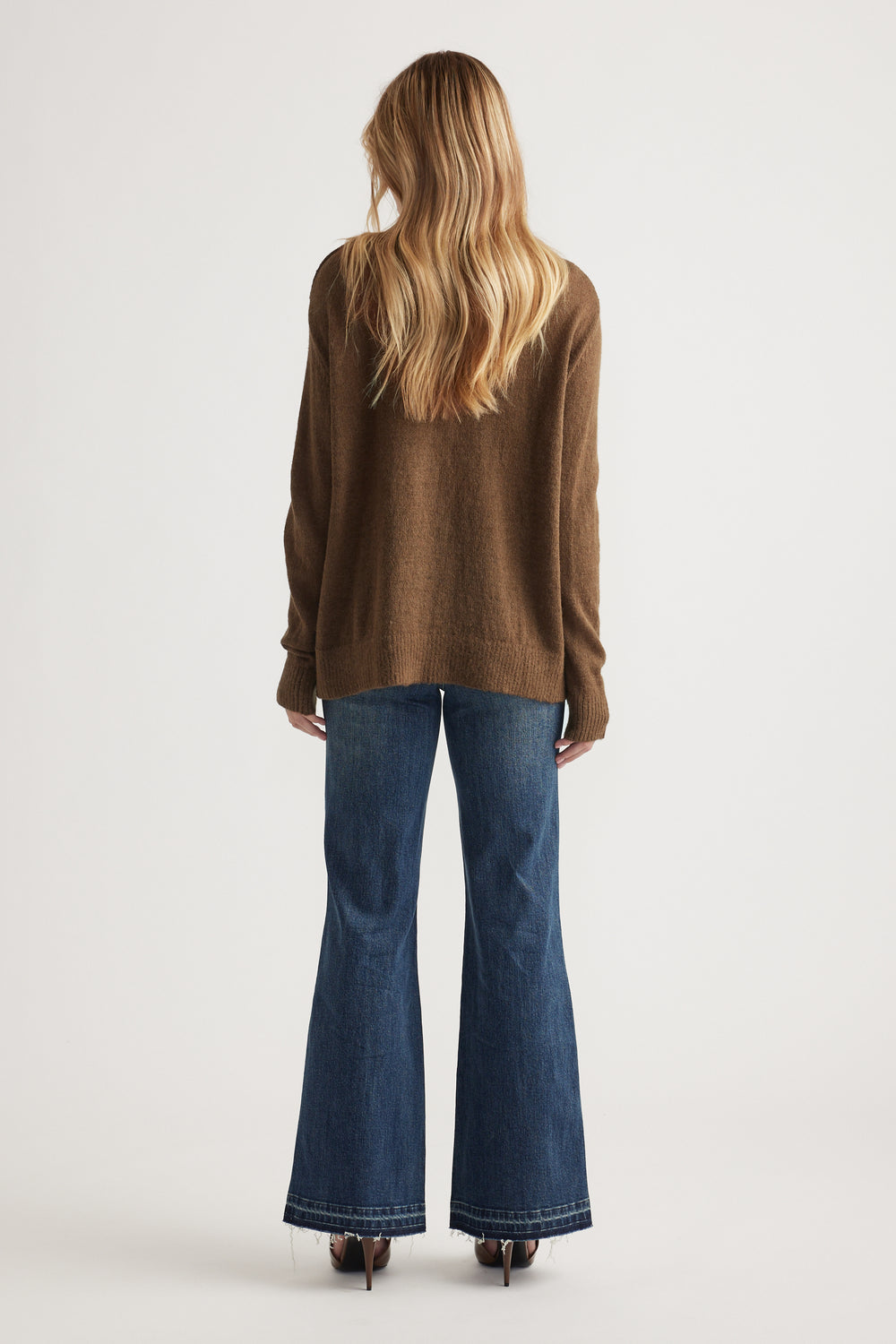 Woman wearing a relaxed brown knit jumper paired with dark blue flared jeans and brown heels, shown from the back.