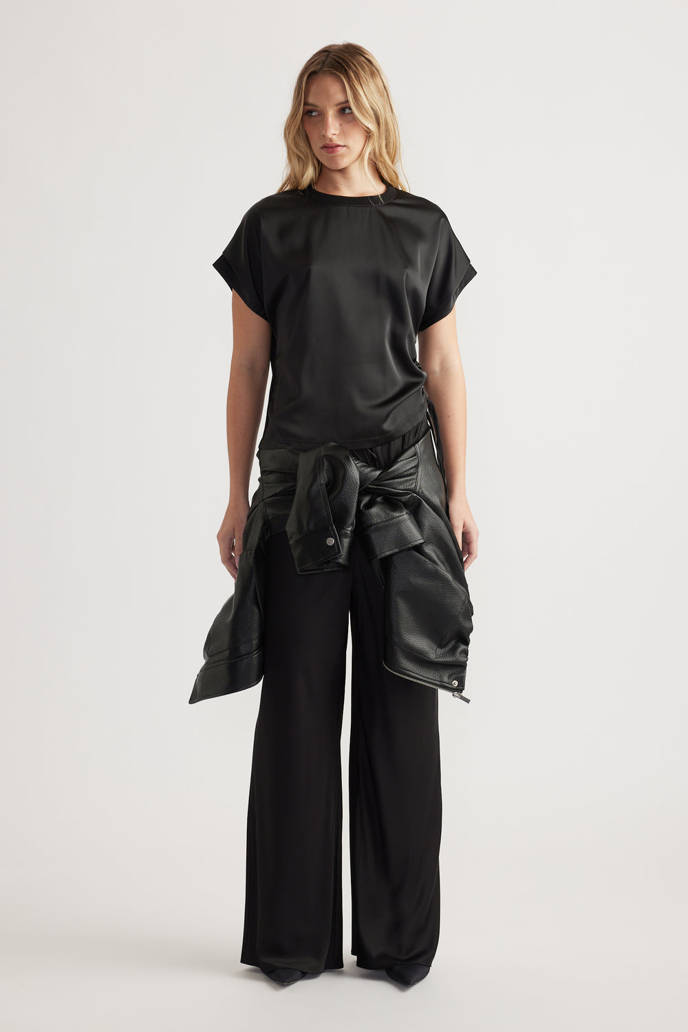 Front view of woman wearing a relaxed fit black satin top with ruched side detail and wide leg black pants