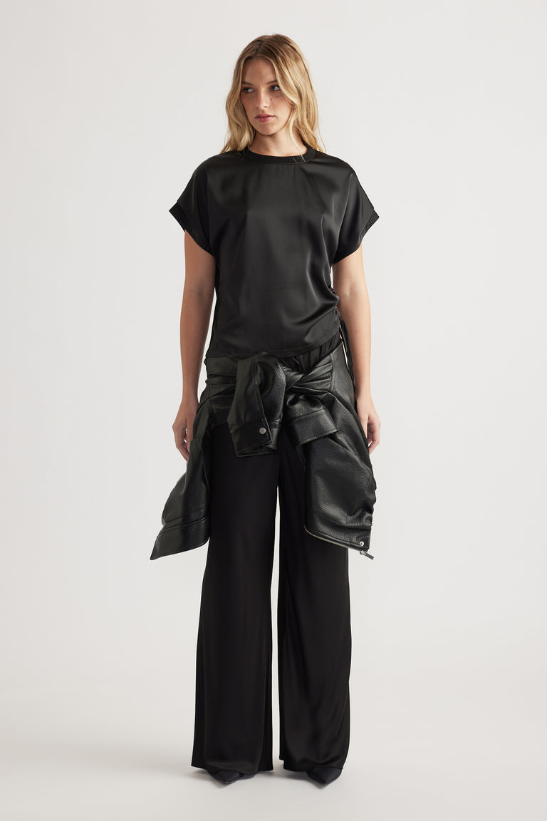 Front view of woman wearing a relaxed fit black satin top with ruched side detail and wide leg black pants