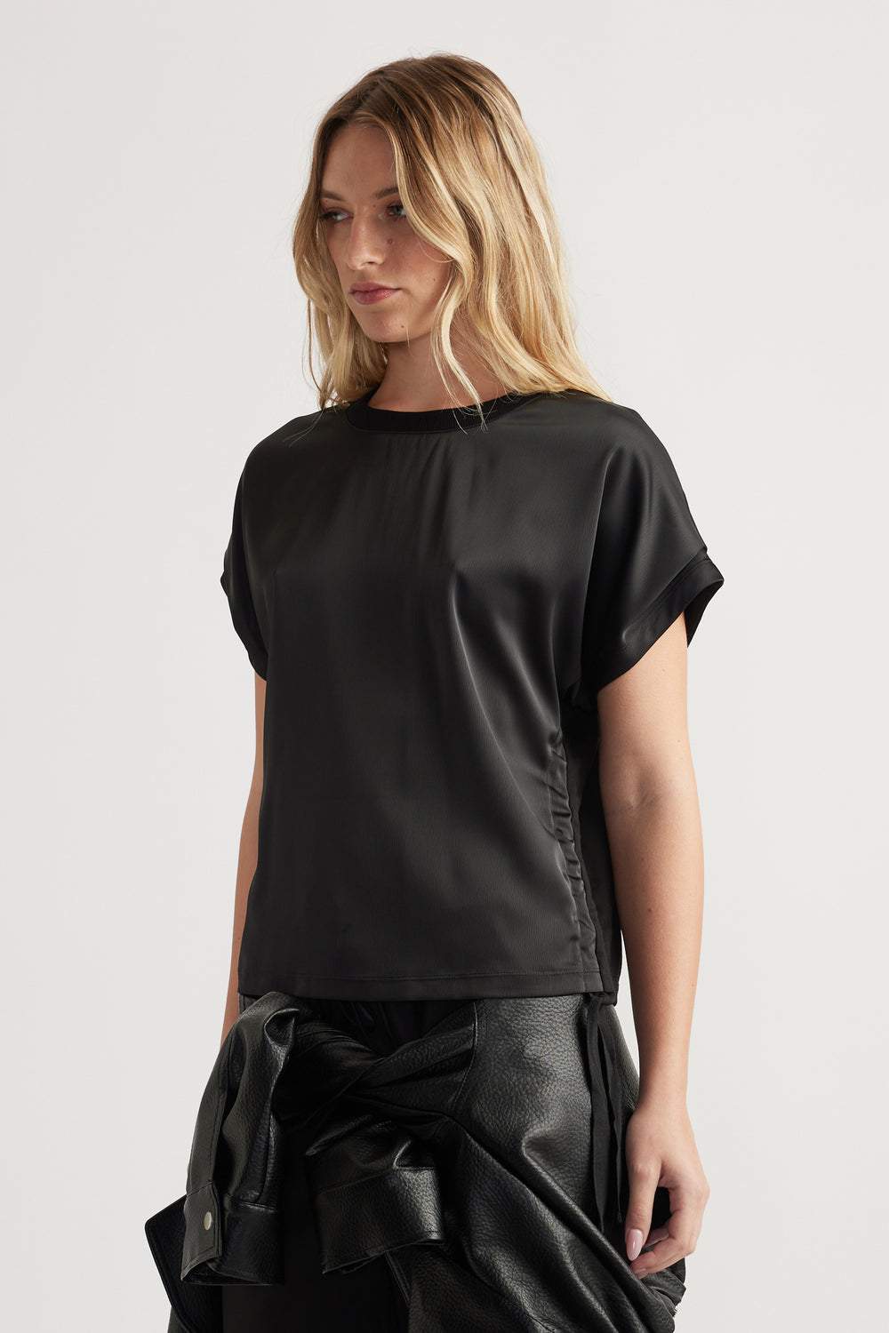 Woman wearing a relaxed fit black satin top with short sleeves and ruched side detail paired with black pants