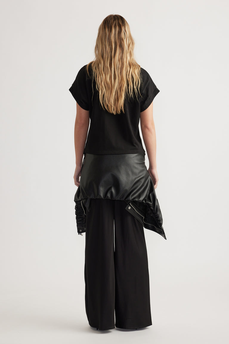 Rear view of woman wearing relaxed fit black short sleeve top with wide-leg black pants and leather jacket tied at waist