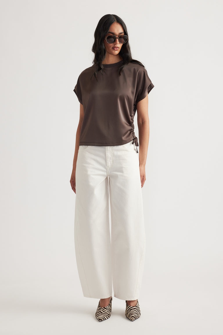 Woman wearing a ruched side tie satin top in dark brown paired with wide-leg white pants and zebra print heels